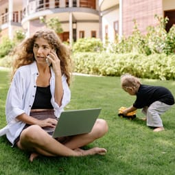 Arbeitende Mutter im Freien mit spielendem Kind