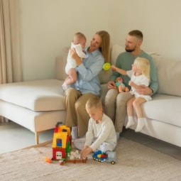 Familie geniesst Spielzeit mit Kindern und Spielzeug auf einem gemütlichen Sofa drinnen.