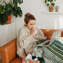 Erkältete Frau liegt auf dem Sofa vor ihrem Laptop