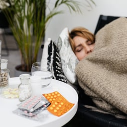 Kranke Frau liegt auf dem Sofa mit Tabletten auf einem Nachtisch