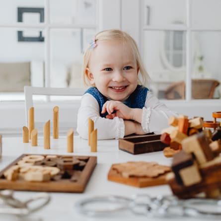 Lächelndes Kleinkind mit blonden Haaren, das an einem Tisch mit Holzspielzeugen spielt Lächelndes Kleinkind mit blonden Haaren, das an einem Tisch mit Holzspielzeugen spielt