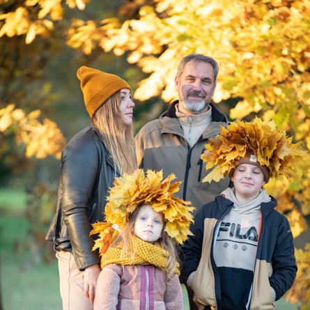 Eine glückliche Familie posiert im Freien im Herbst mit kreativen Blätterkränzen.