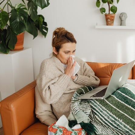 Erkältete Frau liegt auf dem Sofa vor ihrem Laptop